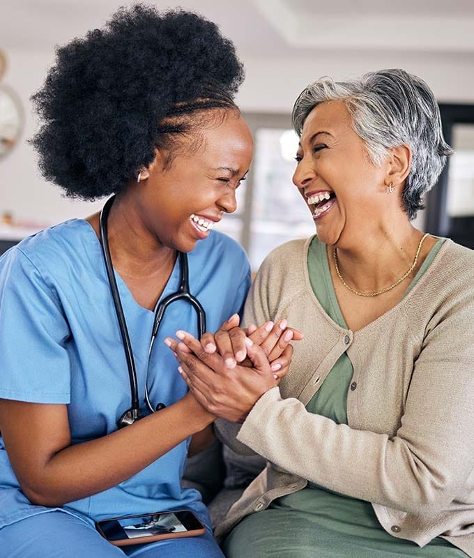 Young nurse and elderly woman holding hands and laughing.
