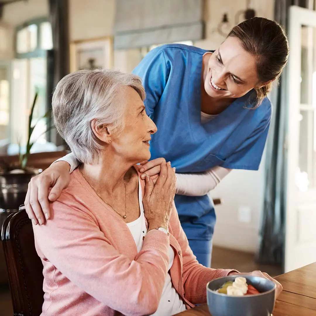 Young nurse smiles at older women, patting her shoulders.