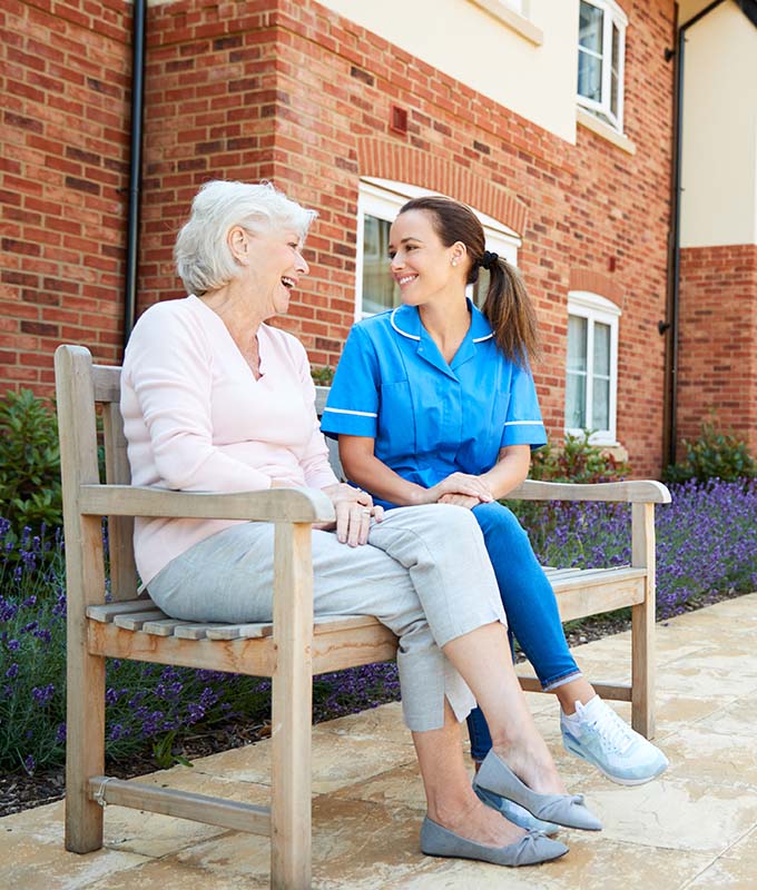 Older woman and young nurse sitting on a bench outside of a building