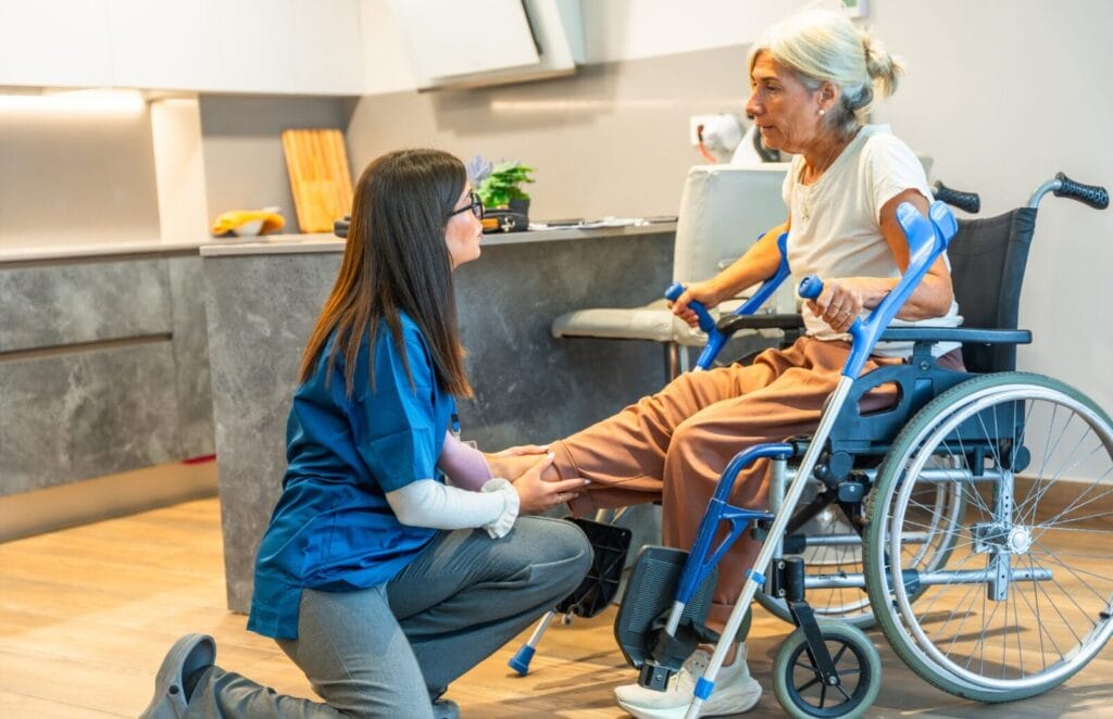 An assisted living caregiver provides physical therapy to a senior woman in a wheelchair.