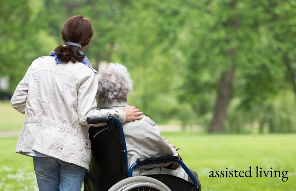 An assisted living caregiver stands with a senior in a wheelchair.
